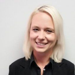 Person mit hellem Haar und einem schwarzen Blazer lächelt in die Kamera.