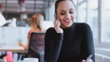 Person telefoniert und lächelt an einem Schreibtisch im Büro.