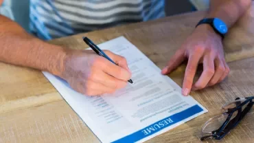 Person schreibt Notizen auf ihren Lebenslauf an einem Tisch.