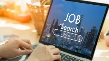 Person tippt auf Laptop mit 'Job Search' auf dem Bildschirm.