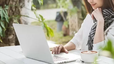 Person arbeitet draußen am Laptop mit Kaffee.