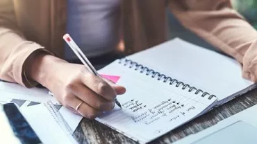Person schreibt Notizen in ein Notebook auf einem Schreibtisch.