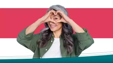 Person formt mit den Händen ein Herz vor einem roten Hintergrund.