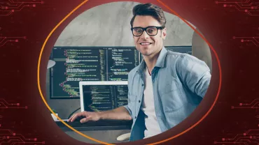 Person mit Brille sitzt vor Computermonitoren mit Code.