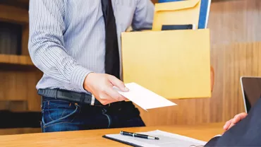 Person mit einem Ordner in der Hand übergibt einen Brief an eine sitzende Person.