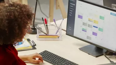 Person arbeitet am Schreibtisch mit Kalender auf dem Computerbildschirm.