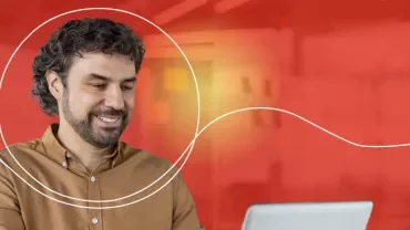 Person arbeitet am Laptop vor rotem Hintergrund.