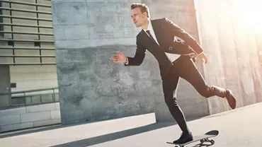 Person in Anzug fährt Skateboard in einer städtischen Umgebung.