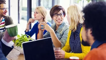 Gruppe von Menschen, die zusammen an einem Tisch mit Laptops und Getränken sitzen.