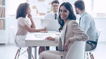Person lächelt im Vordergrund, mit Team im Hintergrund im Büro.