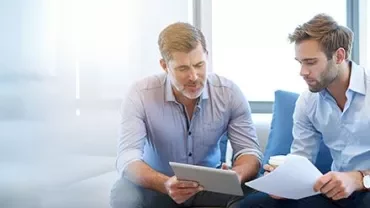 Zwei Personen im Gespräch mit einem Tablet und einem Dokument.