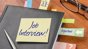 Notizbuch mit einem Zettel 'Job Interview' und farbigen Klebezetteln auf einem Tisch.