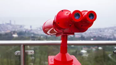Rotes Fernglas auf einem Aussichtspunkt, mit Stadtblick im Hintergrund.