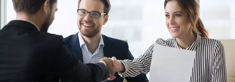 Menschen im Anzug, die sich die Hand schütteln, lächeln.