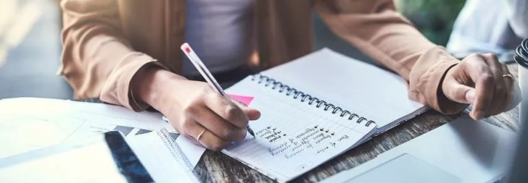 Person schreibt Notizen in ein Notebook auf einem Schreibtisch.