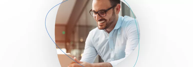 Person mit Brille, lächelnd und auf einen Laptop schauend.