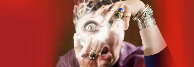 Person mit Schmuck hält eine Lupe vor das Auge, dramatischer Hintergrund.