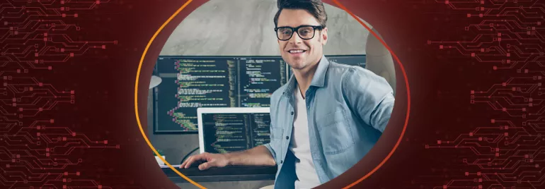 Person mit Brille sitzt vor Computermonitoren mit Code.
