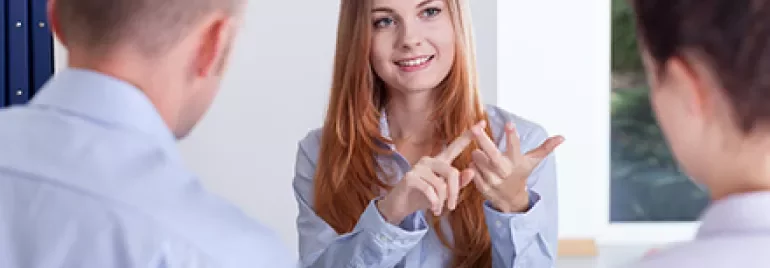 Person sitzt mit zwei anderen an einem Tisch und erklärt etwas, während sie ihre Finger benutzt.