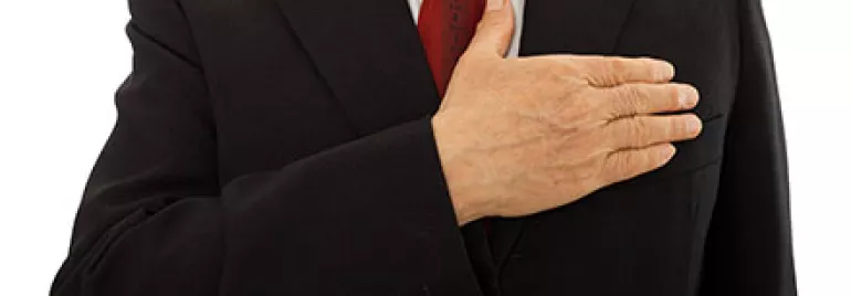 Person in Anzug hält die Hand über der Brust.
