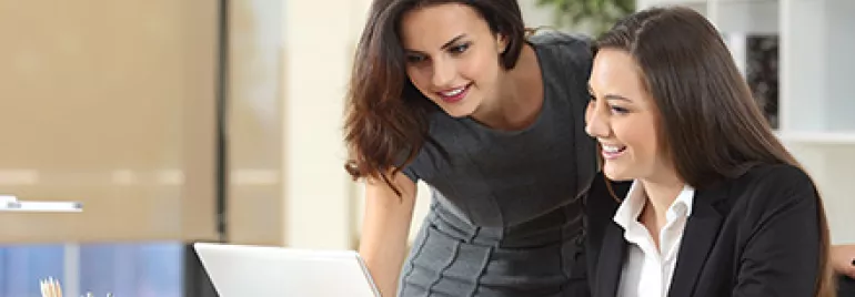 Zwei Personen arbeiten im Büro an einem Laptop.