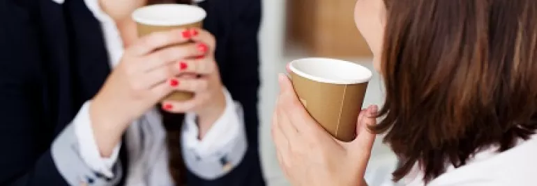 Zwei Personen halten Kaffeebecher und unterhalten sich.
