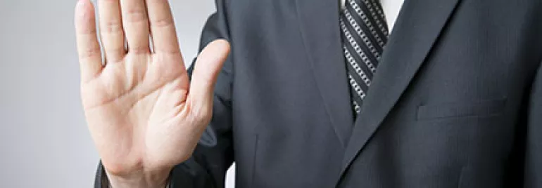 Person im Anzug hebt Hand in Stopp-Geste.
