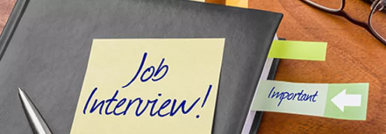 Notizbuch mit einem Zettel 'Job Interview' und farbigen Klebezetteln auf einem Tisch.