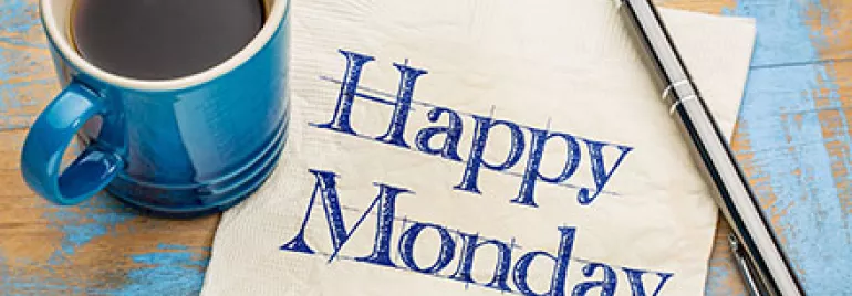 Blaue Tasse Kaffee neben Serviette mit 'Happy Monday'.