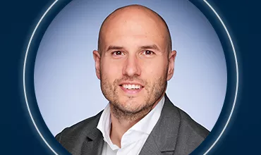 Porträtfoto einer Person mit Glatze vor blauem Hintergrund.