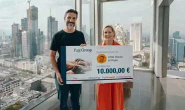 Zwei Personen halten einen großen Spendenscheck mit Stadtblick im Hintergrund.