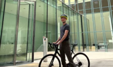 Person mit Fahrrad vor einem modernen Glasgebäude.