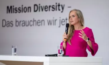 Person hält eine Rede auf einer Bühne mit Mikrofon.