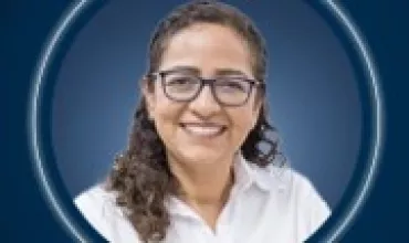 Lächelnde Person mit Brille und lockigem Haar vor blauem Hintergrund.
