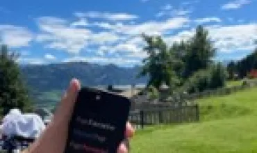 Hand hält ein Smartphone im Freien mit blühender Landschaft im Hintergrund.