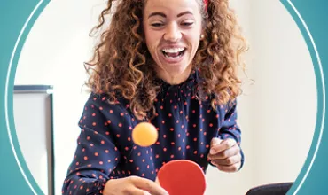 Person spielt Tischtennis und lacht.