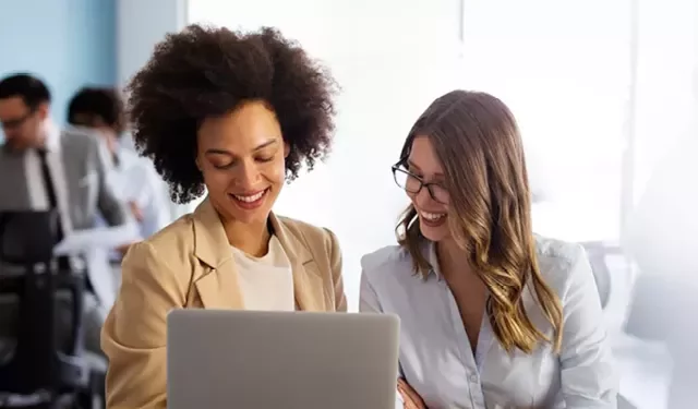 Zwei Personen, die an einem Laptop arbeiten und lächeln.